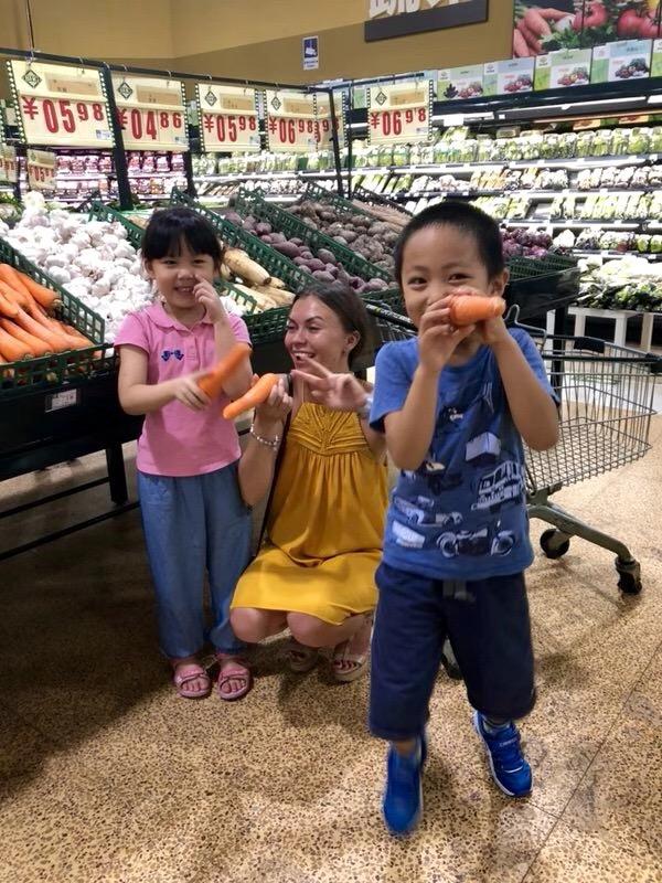 Alisa with two children holding carrots in a supermarket, practising vocabulary